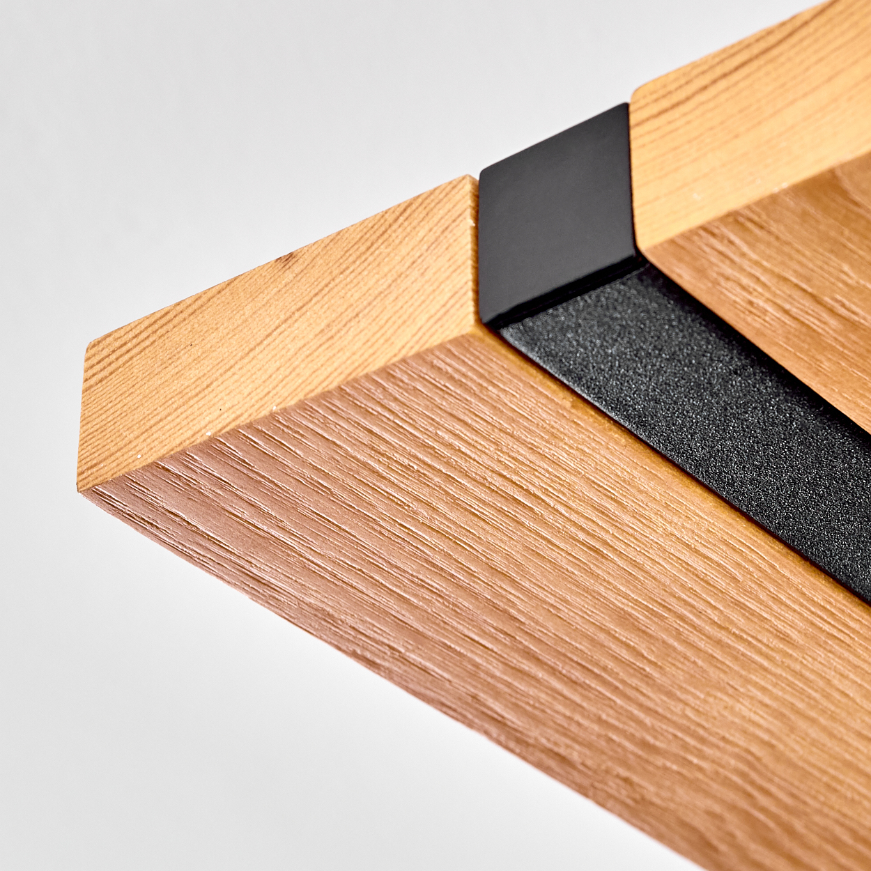 Nahaufnahme eines Holzbalkens mit schwarzem Metallwinkel. Helle Holzmaserung kontrastiert mit dunklem Metall auf weißem Hintergrund.