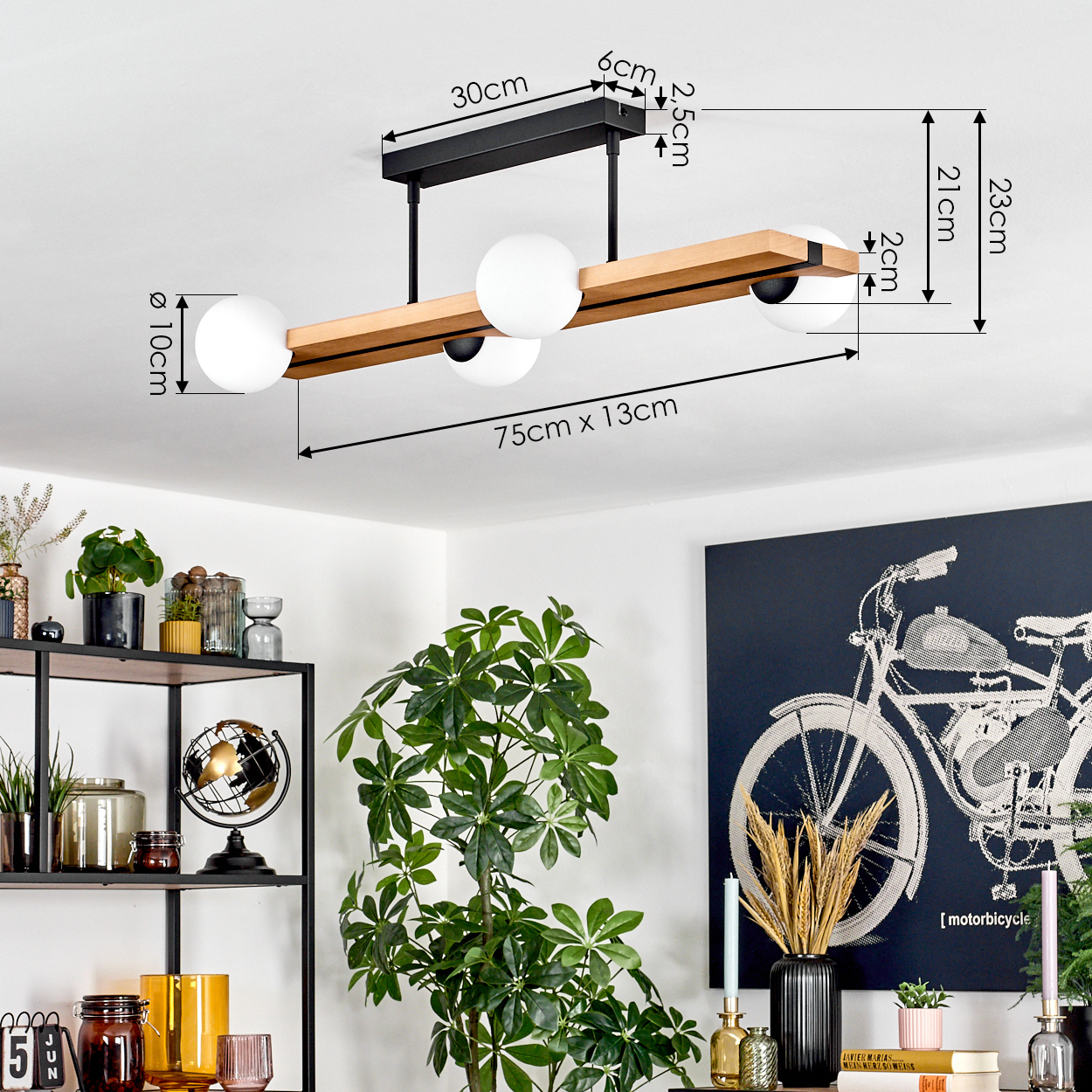 Eine moderne Deckenlampe mit drei weißen Kugeln und einem Holzbalken. Maße sind angegeben. Dekorative Elemente sind im Hintergrund.