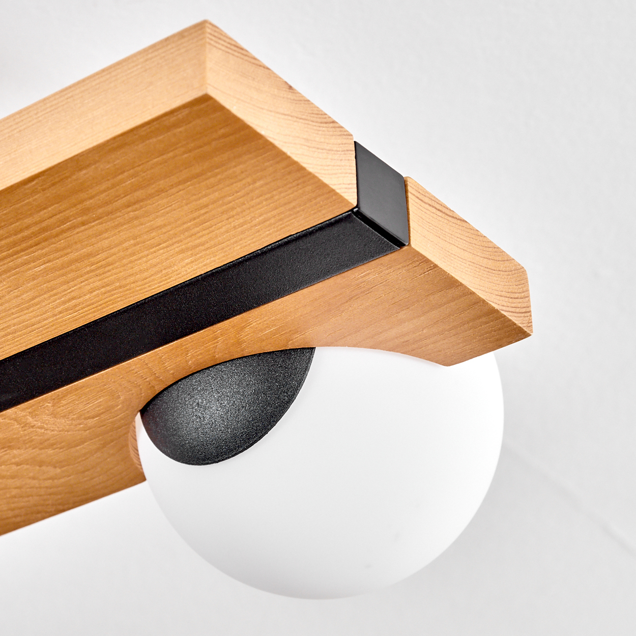 Nahaufnahme einer modernen Leuchte. Sie hat einen Holzbalken, einen schwarzen Metallakzent und ein weißes, kugelförmiges Licht.
