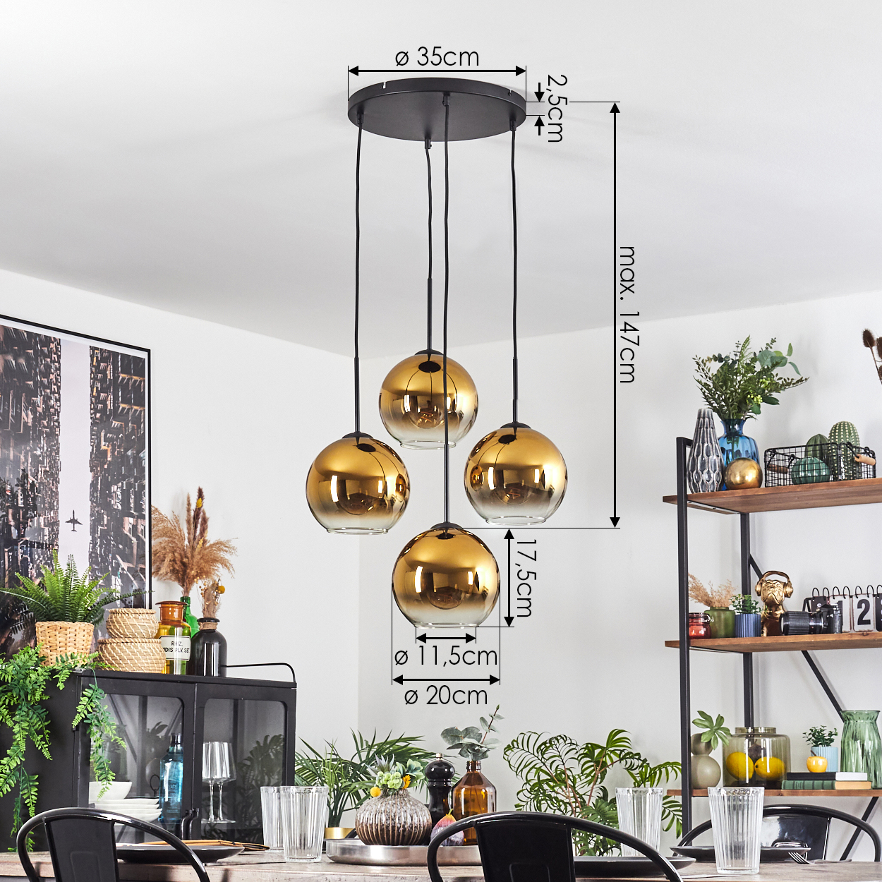 Eine Pendelleuchte mit vier goldfarbenen Kugeln hängt über einem Esstisch mit Gläsern und Pflanzen. Im Hintergrund ein Regal mit Dekoration.