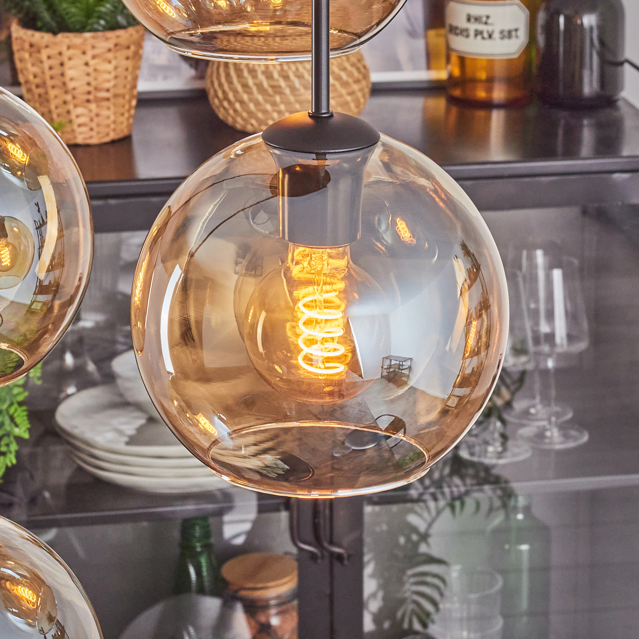 Nahaufnahme einer Glaskugel-Leuchte mit Wendelglühbirne. Andere Lichter und Dekorationen sind im unscharfen Hintergrund.
