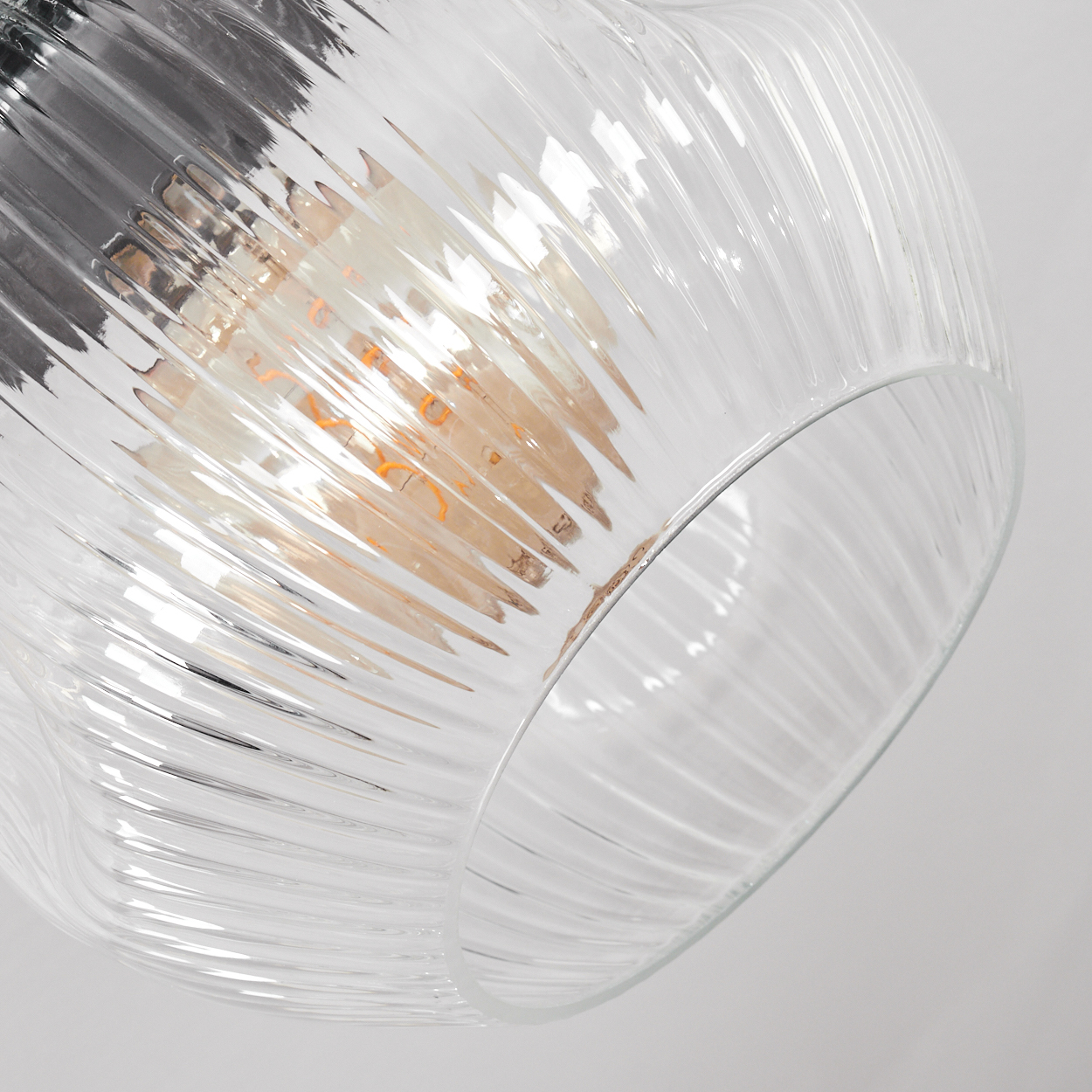 Ein klarer Lampenschirm mit gerilltem Design. Im Inneren leuchtet eine Glühbirne. Der Hintergrund ist ein schlichtes Weiß.