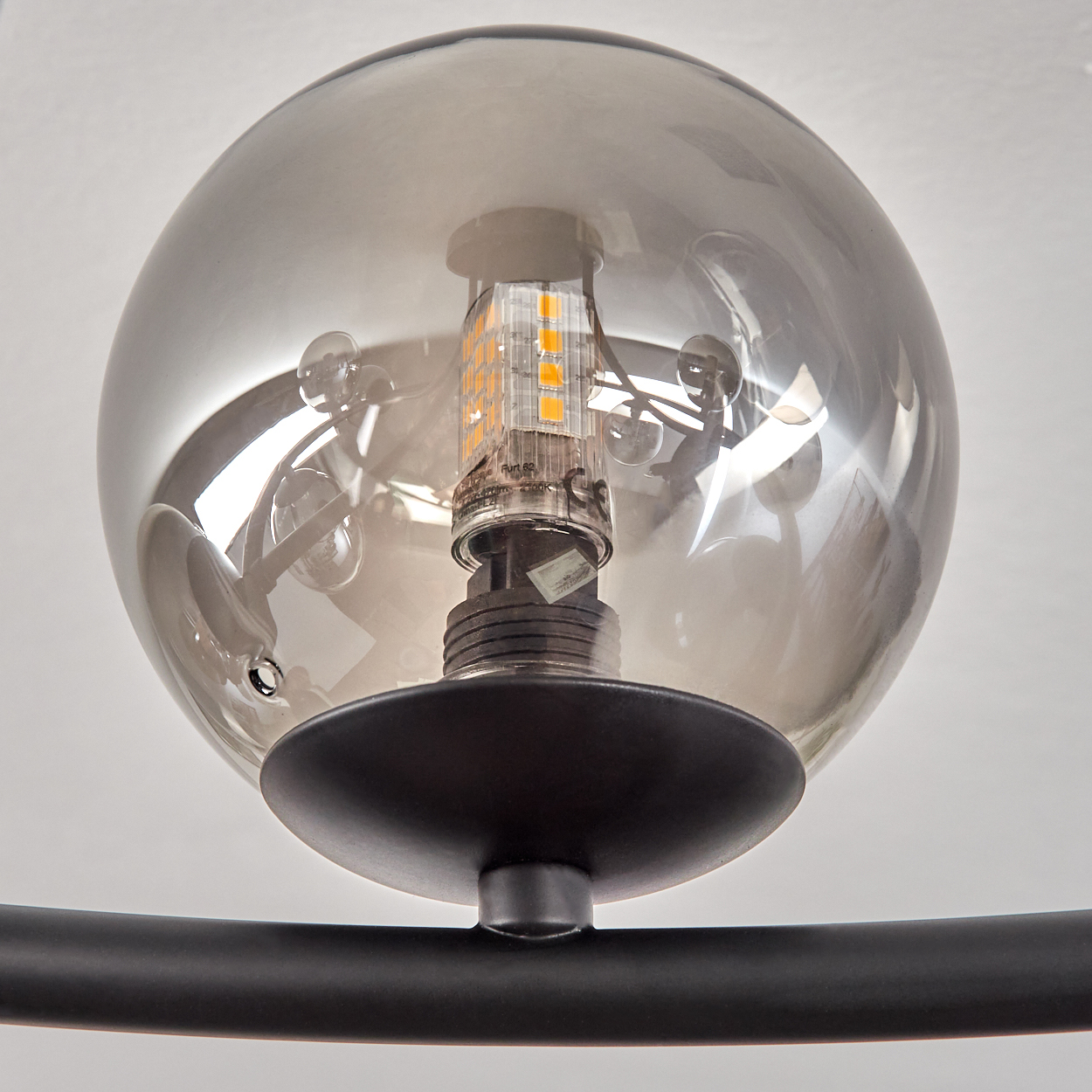 Nahaufnahme einer modernen Leuchte. Sie hat einen rauchigen Glaskolben, eine warmtonige LED und eine schwarze Metallhalterung.