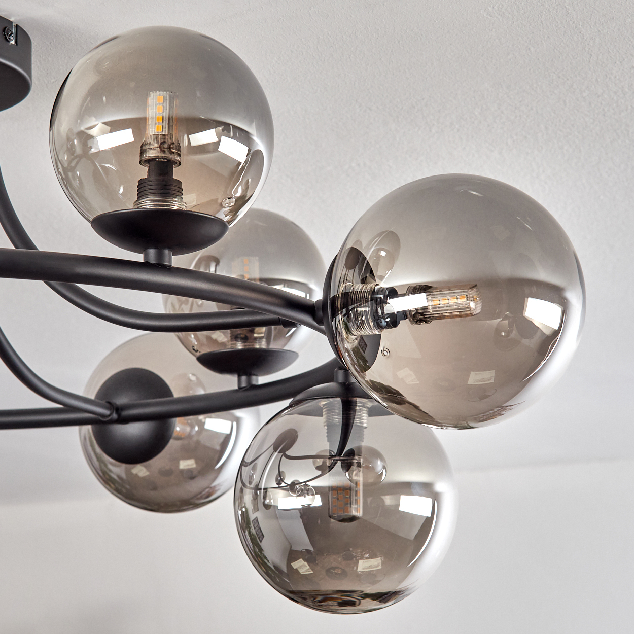 Eine moderne Deckenleuchte mit mehreren rauchfarbenen Glaskugelschirmen und schwarzen Metallarmen. Die Glühbirnen sind in den Kugeln sichtbar.