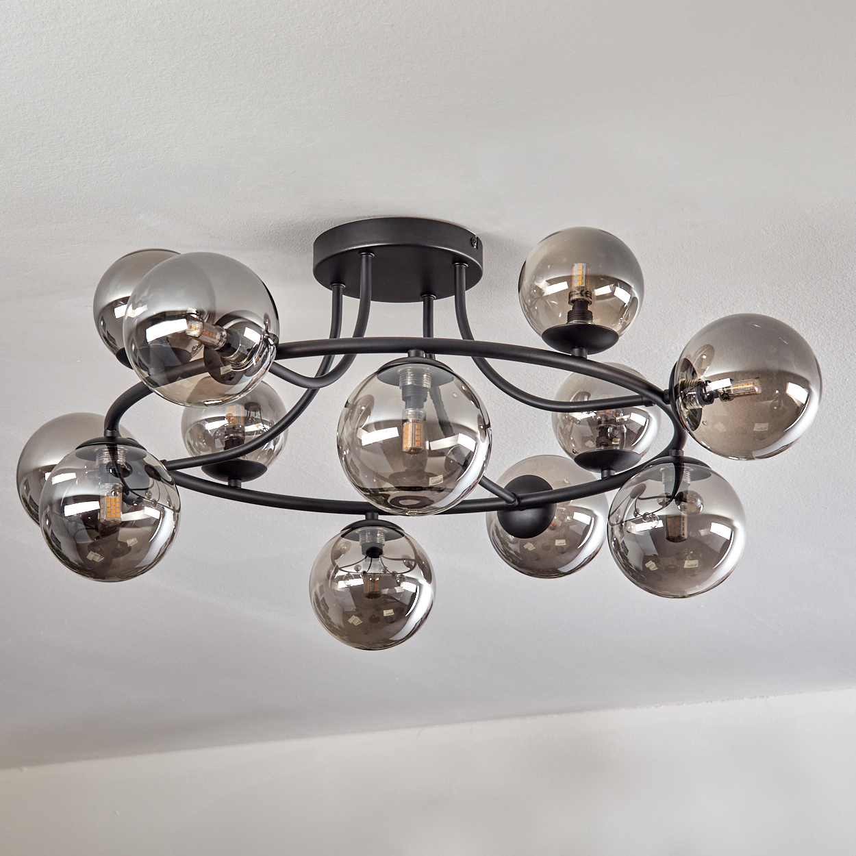 Eine moderne Deckenleuchte mit runden, rauchfarbenen Glaskugeln. Sie hat einen schwarzen Metallrahmen und ist an einer weißen Decke befestigt.