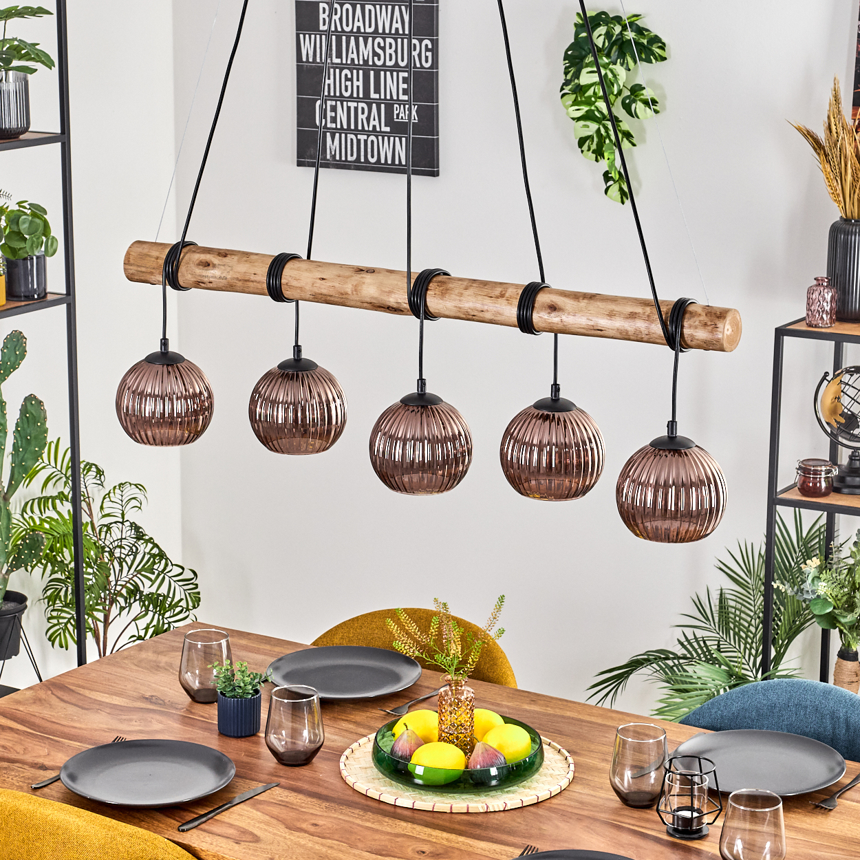 Ein Esszimmer mit Holztisch, Lampen und einem Obstteller. Teller, Gläser und Stühle sind ebenfalls vorhanden. Ein Broadway-Schild hängt.