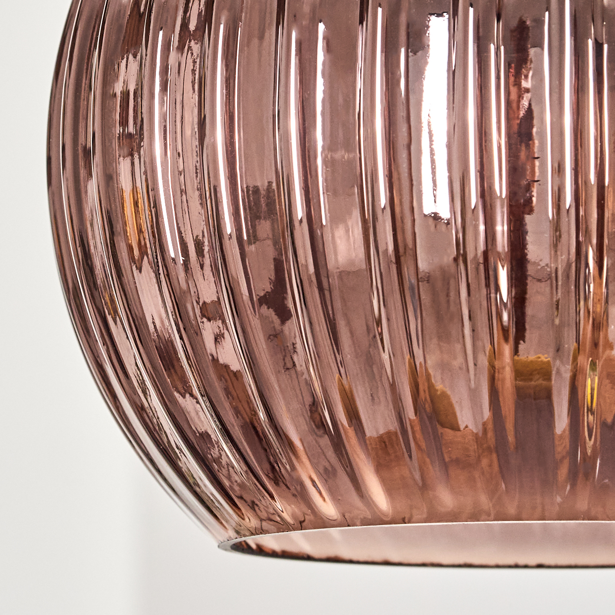 Nahaufnahme eines roségoldenen Glasobjekts. Es hat vertikale Rillen und reflektiert Licht, wodurch Glanzlichter entstehen. Weißer Hintergrund.