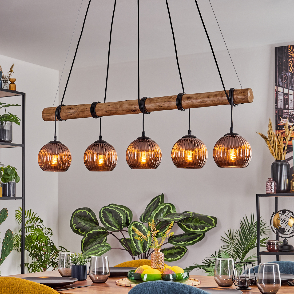 Esszimmer mit Holzbalken-Kronleuchter. Fünf Glaslampen hängen über einem Tisch mit Gläsern und Pflanzen.