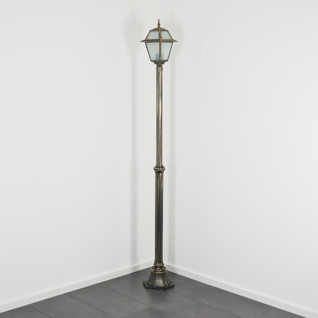 Eine dekorative, antike Straßenlaterne steht in einer Ecke. Sie hat eine Bronzefinish, mit einem Glasgehäuse oben. Der Hintergrund ist weiß.