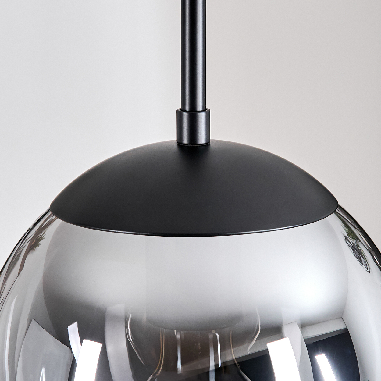 Nahaufnahme einer modernen Pendelleuchte. Sie hat einen schwarzen Metallaufsatz und -schaft mit einem transparenten, grauen, kugelförmigen Glasschirm.