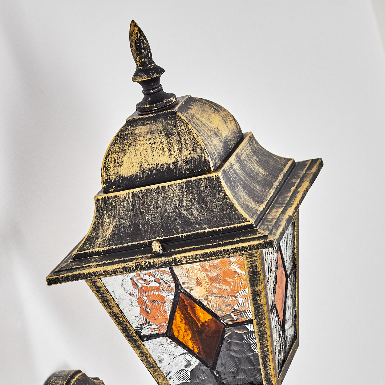 Nahaufnahme einer schwarzen und goldenen Vintage-Laterne mit Buntglasscheiben. Der Hintergrund ist weiß.