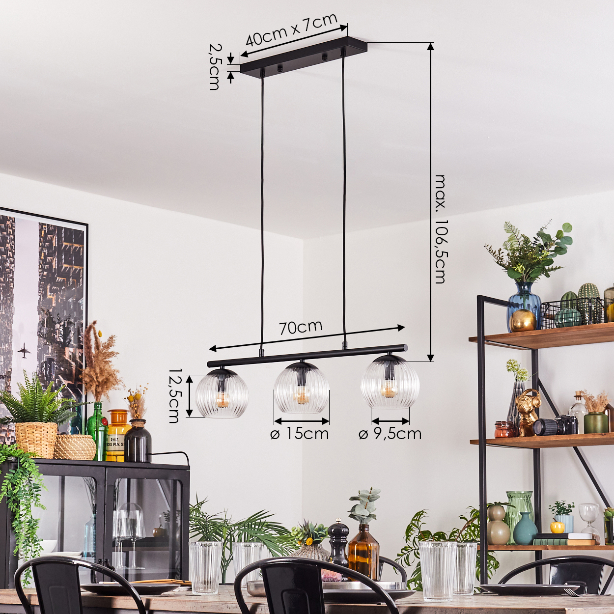 Eine moderne schwarze Hängelampe mit drei Glaskugeln hängt über einem Holztisch. Abmessungen sind angegeben. Regale mit Dekoration sind im Hintergrund sichtbar.