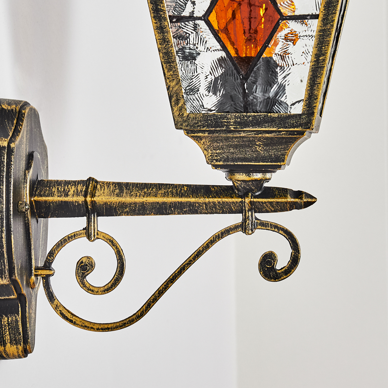Eine dekorative Wandlampe mit goldenem Rahmen und Buntglasaufsatz, an einer weißen Wand befestigt. Die Lampe hat ein Vintage-Design.