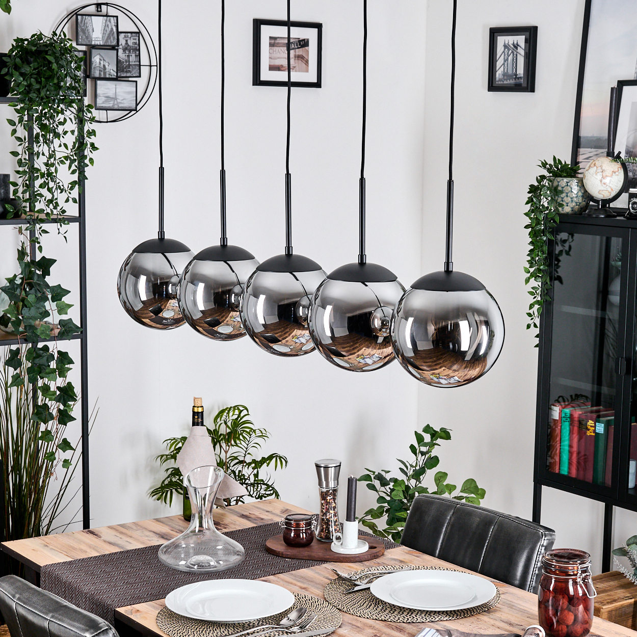 Esszimmer mit Holztisch, hängenden Kugelleuchten und Tischdeko. Pflanzen und Deko im Hintergrund.