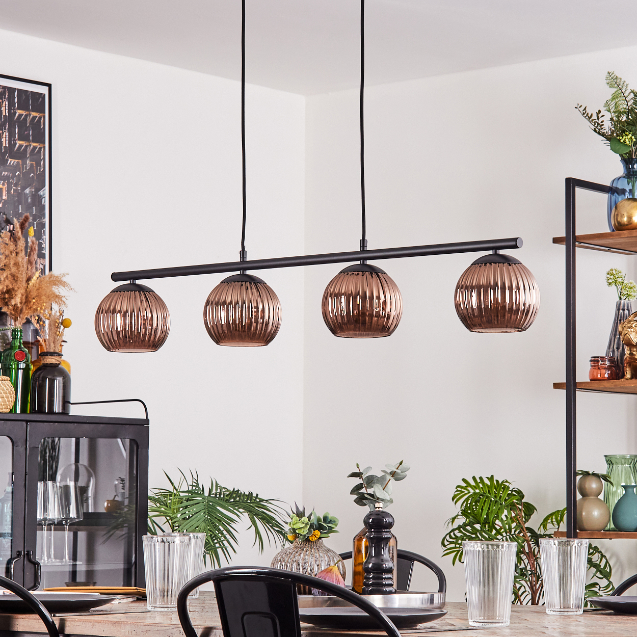 Esszimmer mit Holztisch, schwarzen Stühlen und kupferfarbenen Pendelleuchten. Pflanzen und Dekorationen füllen den Raum.