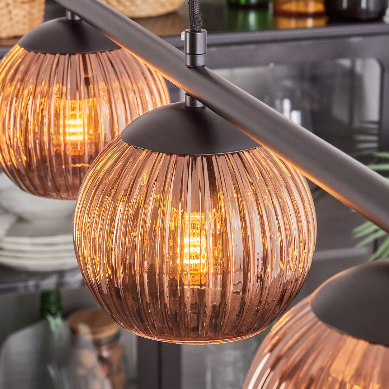 Nahaufnahme einer modernen Leuchte mit drei kugelförmigen, gerippten Glasschirmen. Jeder Schirm hat ein warmes, glühendes Licht.