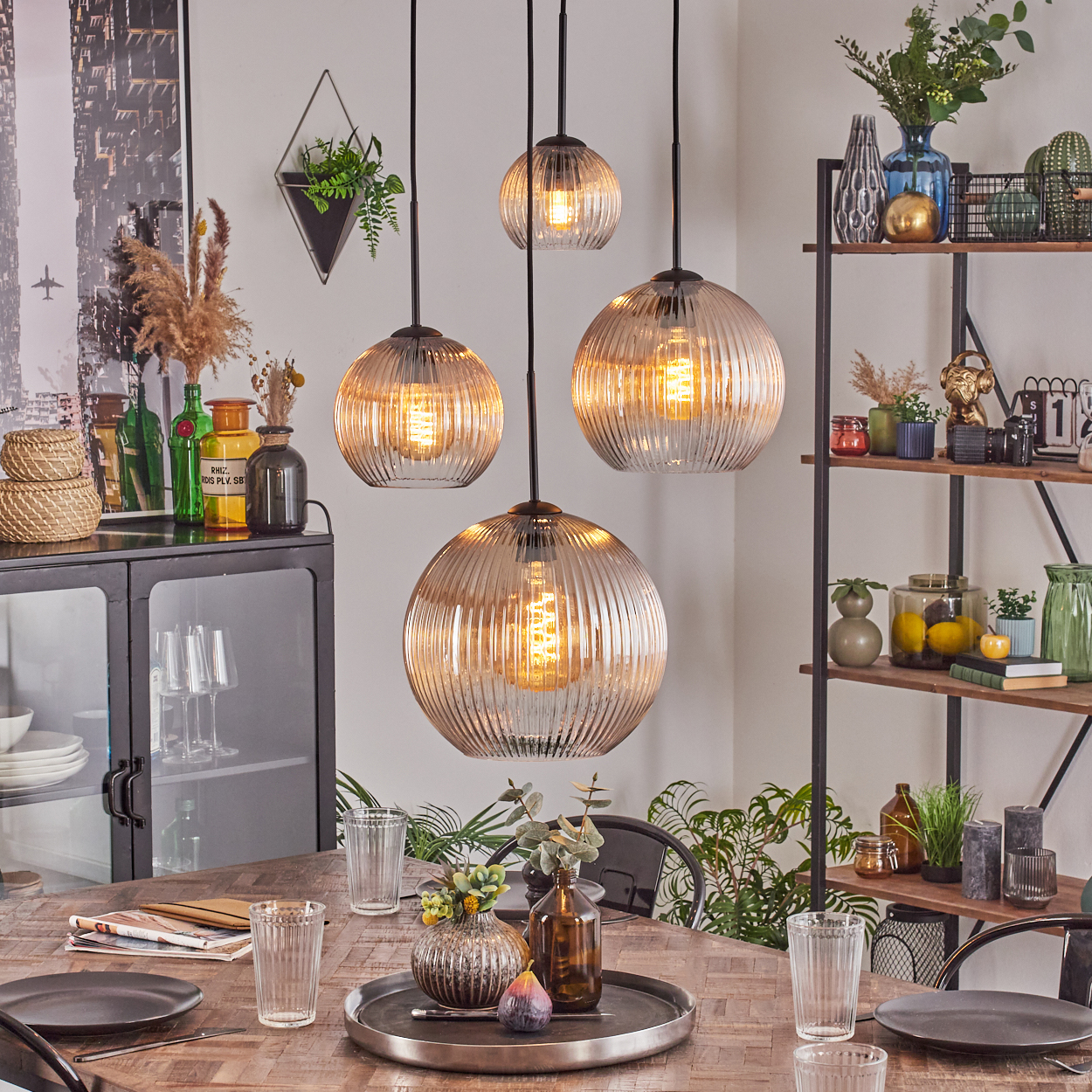 Esszimmer mit Hängelampen. Tisch mit Tellern und Gläsern. Regale und Schrank mit Dekorationen und Pflanzen.