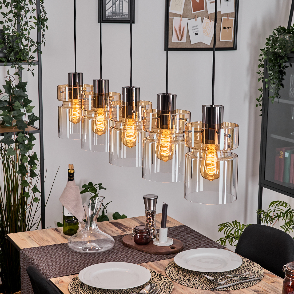 Esszimmer mit Holztisch. Hängelampen über dem Tisch. Teller, Weinflasche und Karaffe stehen auf dem Tisch.