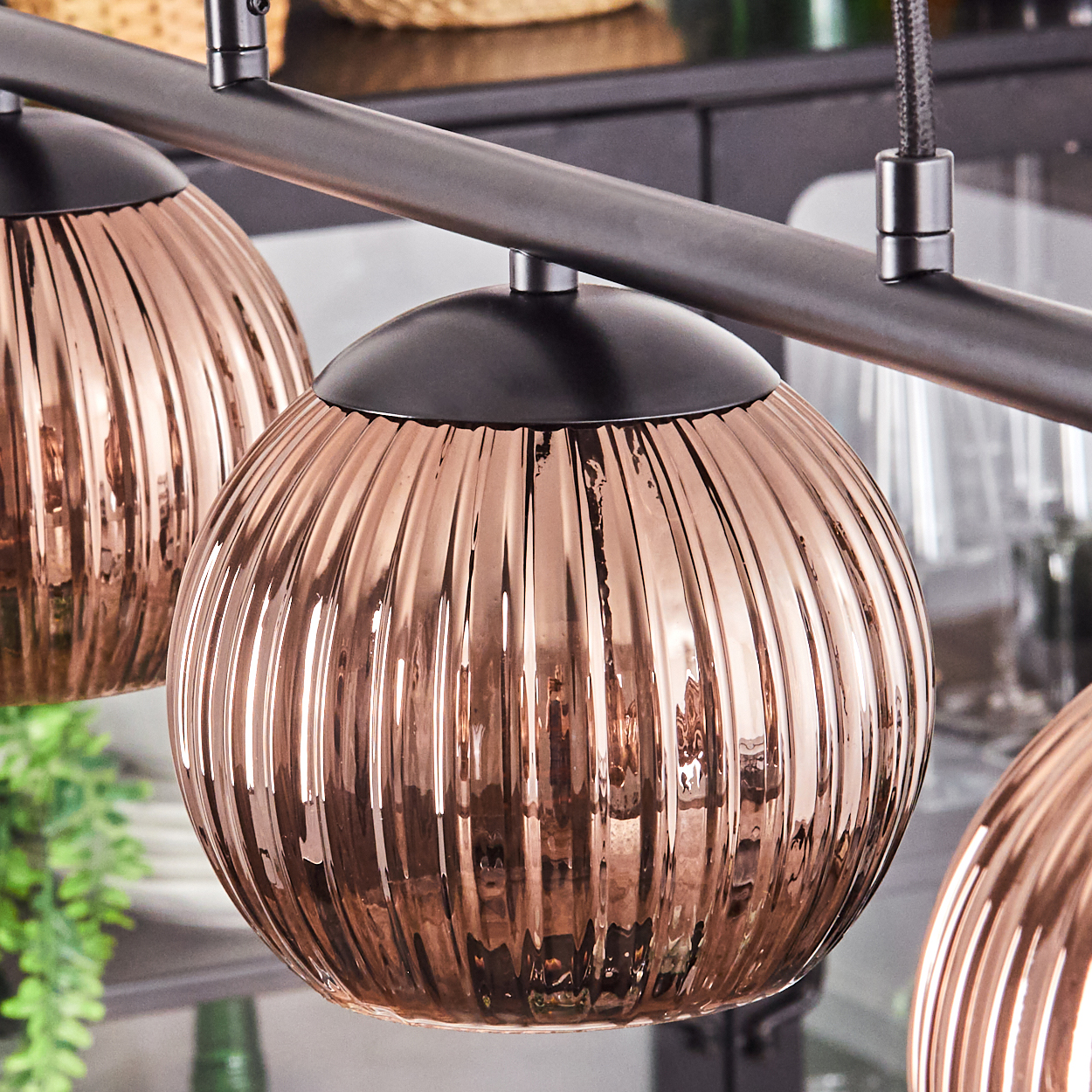 Nahaufnahme einer modernen Leuchte mit drei kupferfarbenen, gerippten Glaskugeln, die an einer dunklen Metallstange hängen.