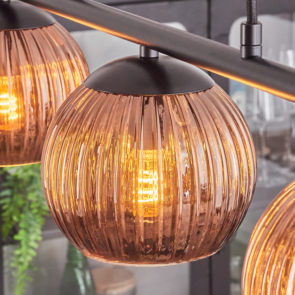 Nahaufnahme einer modernen Leuchte mit drei kugelförmigen, gerippten Glasschirmen, jede mit einer hellen Glühbirne. Die Schirme sind bronze.