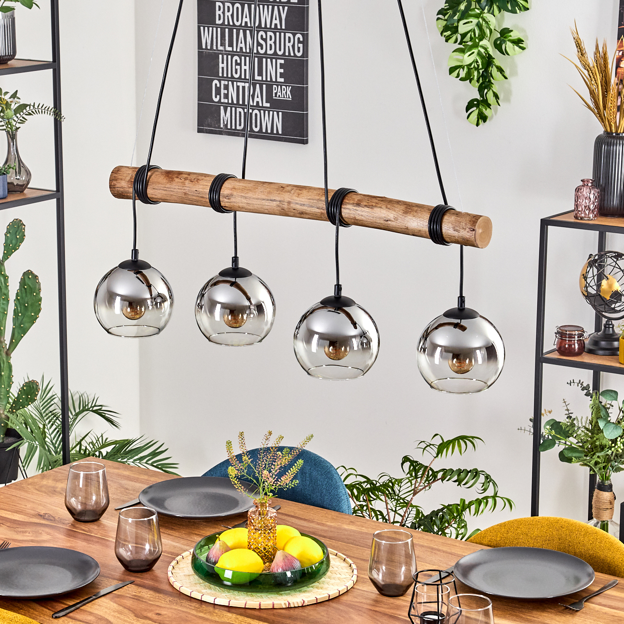 Ein Esszimmer mit Holztisch, vier silbernen Pendelleuchten, Tellern und Gläsern. Ein Schild an der Wand lautet 'Broadway'.