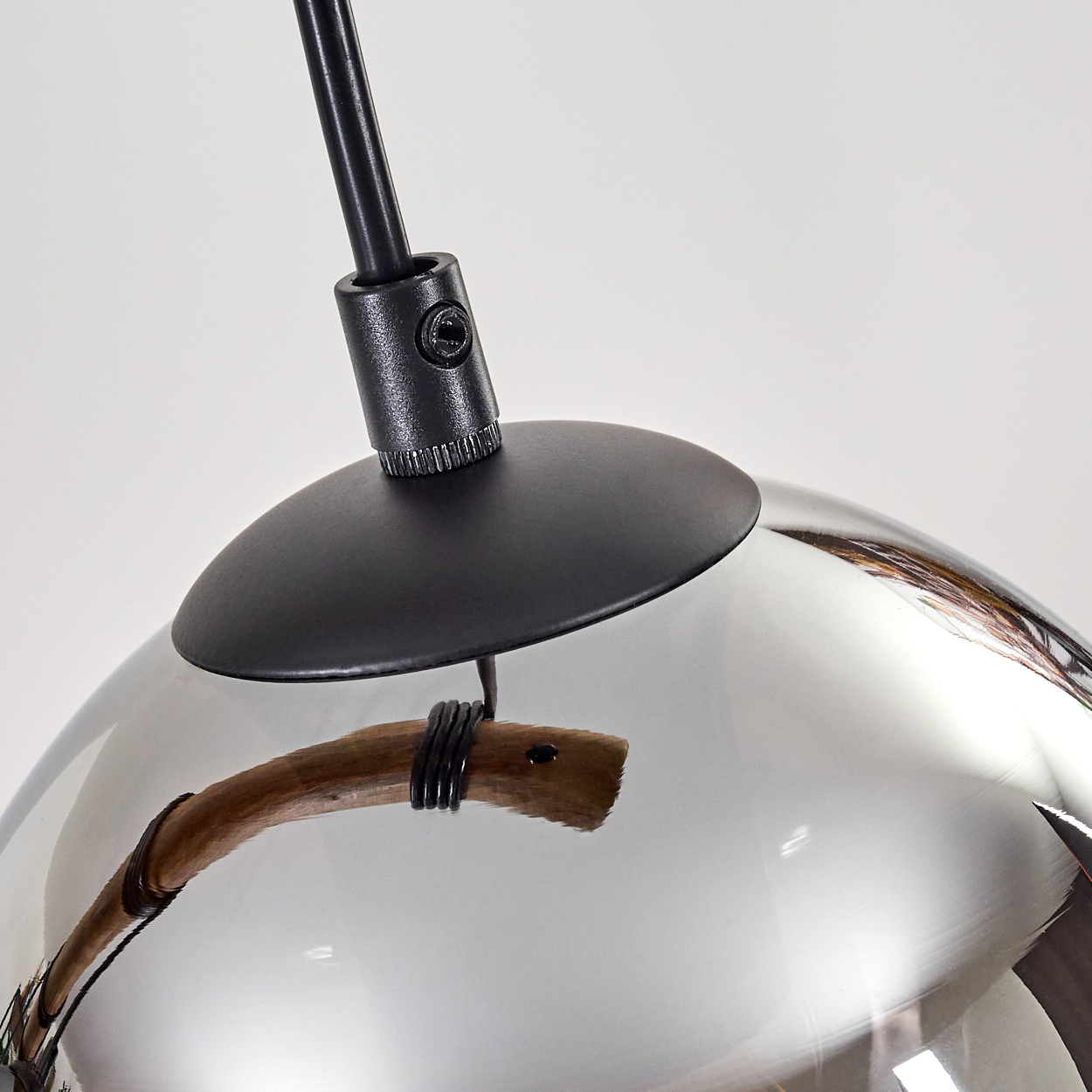 Nahaufnahme einer modernen Leuchte. Sie hat einen schwarzen Stiel, eine schwarze kreisförmige Basis und eine reflektierende Glaskugel mit Holzakzent.