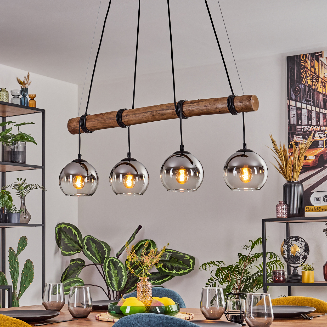 Esszimmer mit Holzbalken-Kronleuchter. Vier kugelförmige Lampen hängen herunter. Tisch mit Gläsern und Pflanzen gedeckt. Ein Gemälde an der Wand.