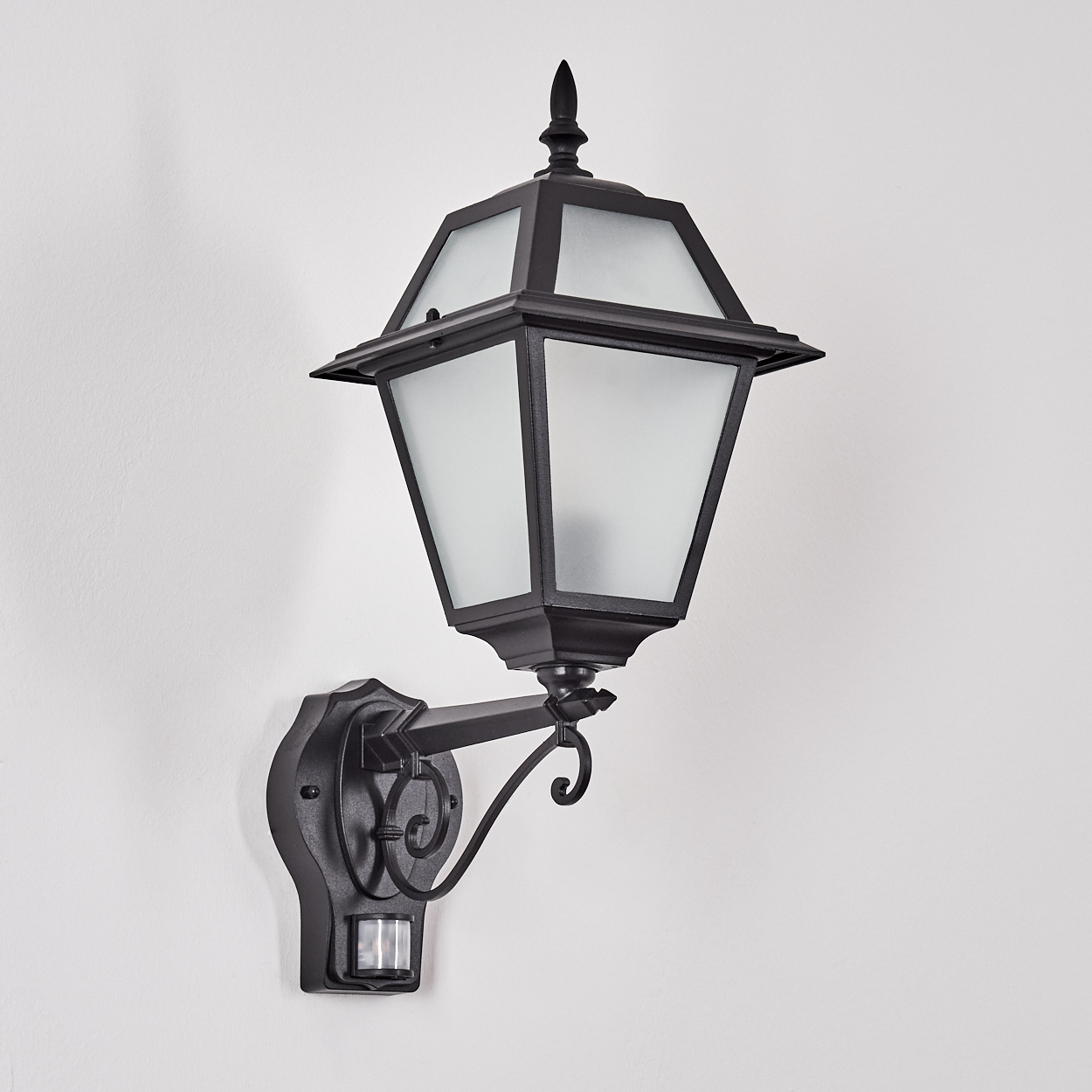 Schwarze Außenlampe mit mattierten Glasscheiben, an einer weißen Wand befestigt. Die Lampe hat einen Bewegungssensor.