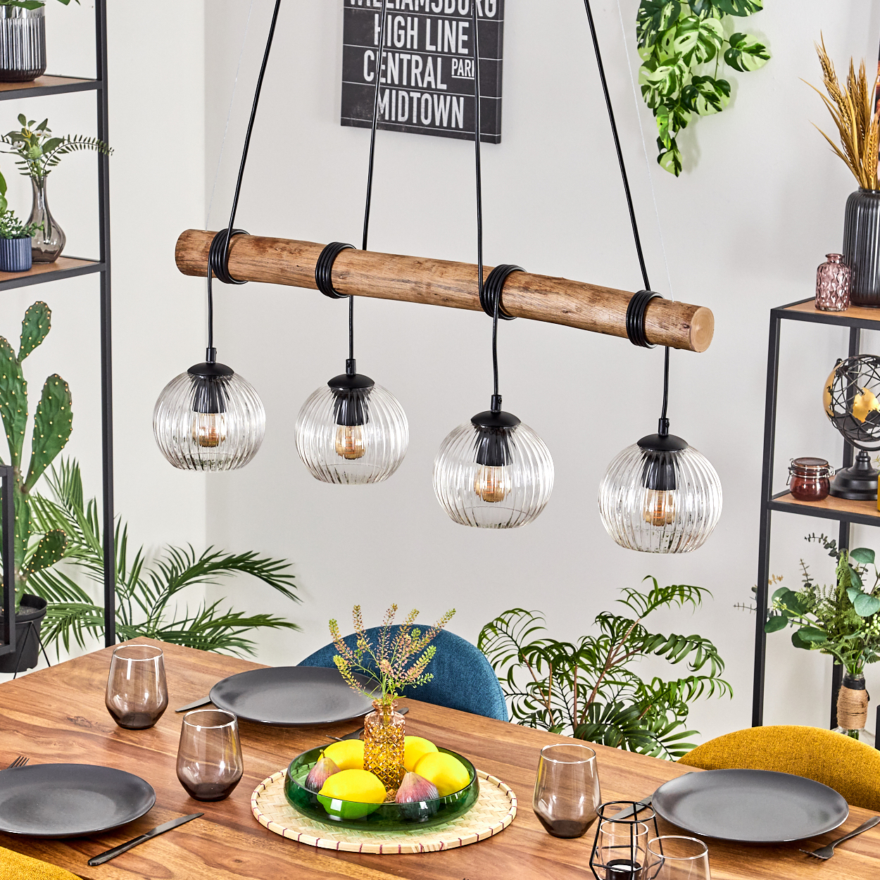 Ein Esszimmer mit Holztisch, vier Kugellampen, einer Obstschale. Pflanzen und Regale sind sichtbar.