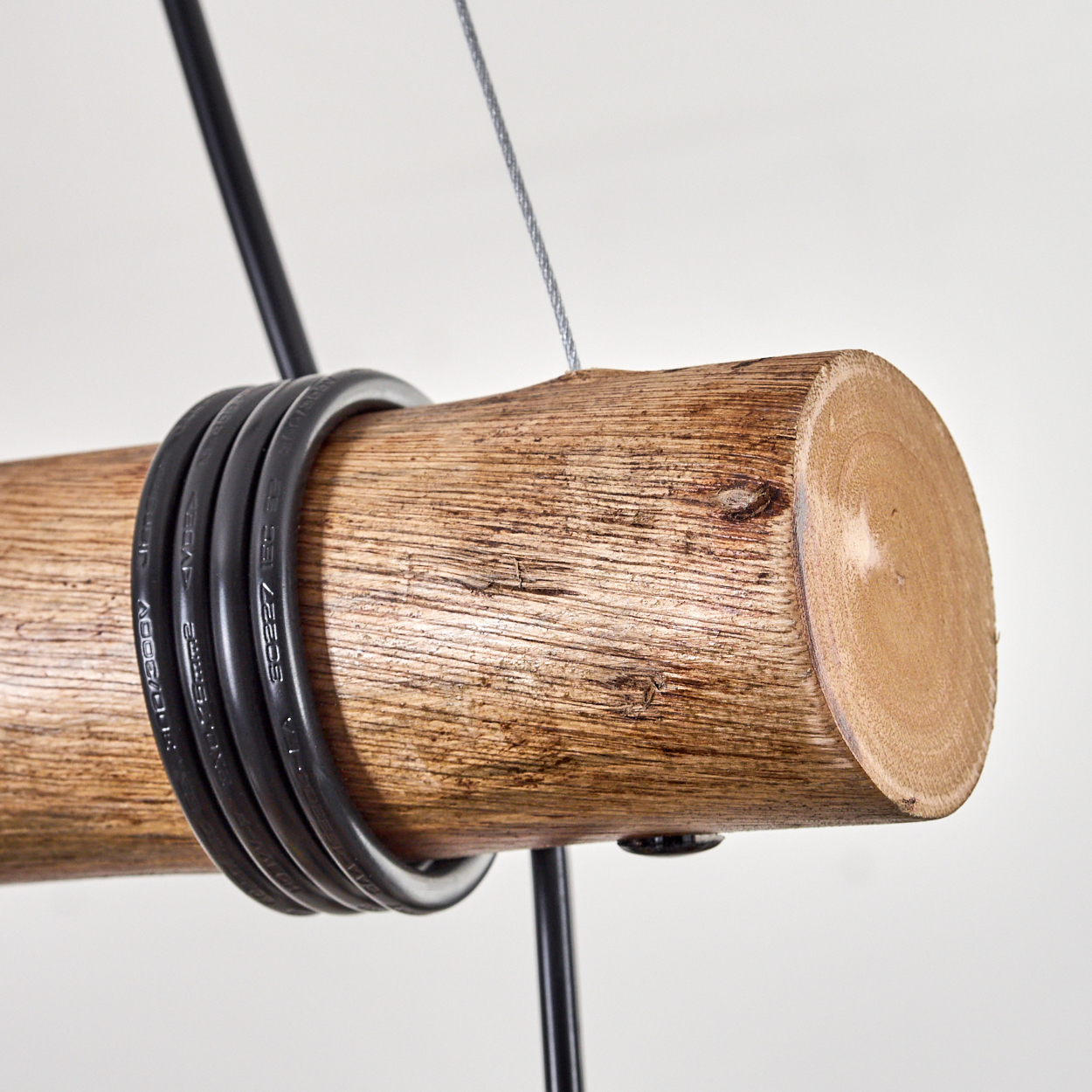 Nahaufnahme eines Holzstamms mit schwarzen Kabeln. Ein silbernes Kabel und schwarze Metallstangen stützen den Stamm vor weißem Hintergrund.