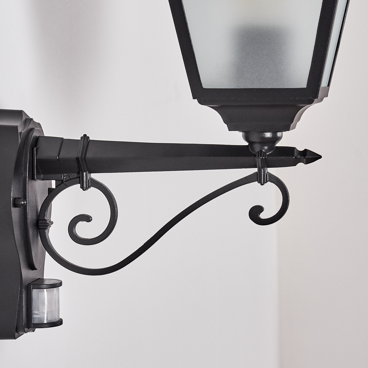 Eine schwarze Außenlampe mit Sensor. Sie hat eine dekorative Halterung und einen Schirm aus Milchglas.