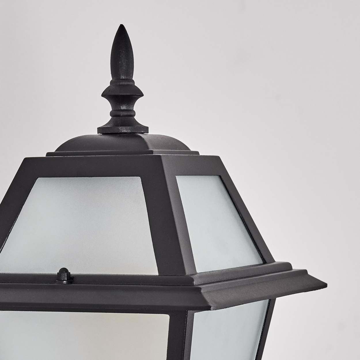 Nahaufnahme einer schwarzen Außenlampe. Sie hat eine spitze Oberseite, eine geometrische Form und Milchglasscheiben auf weißem Hintergrund.
