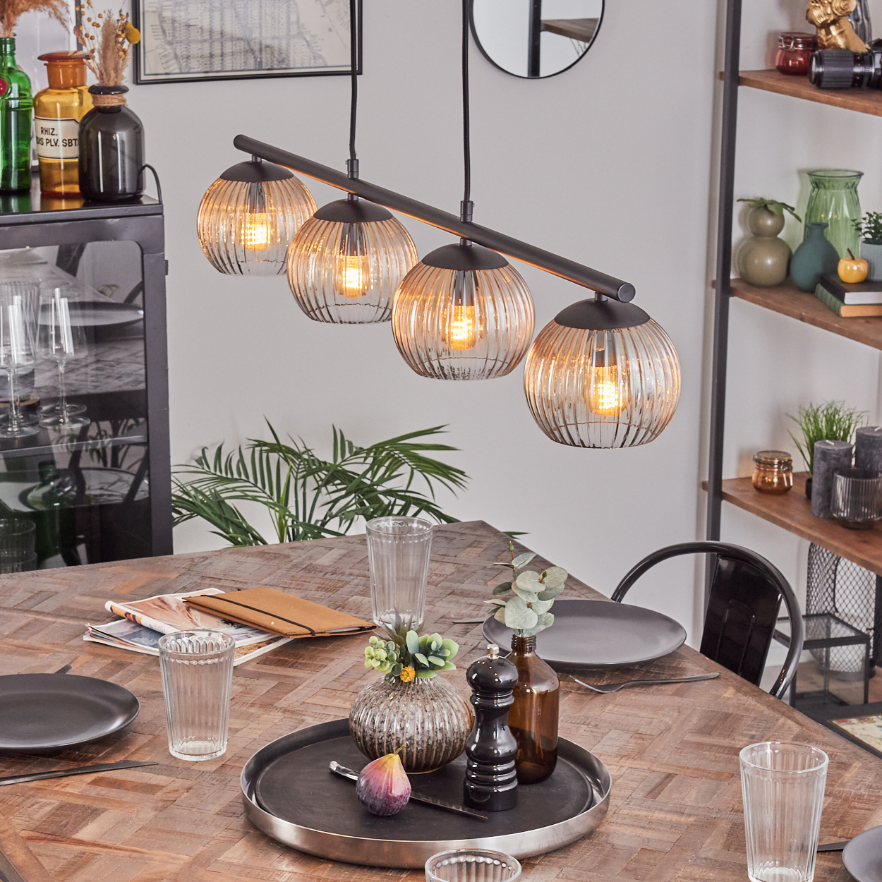 Esszimmer mit Holztisch, gedeckt für eine Mahlzeit, vier Pendelleuchten und verschiedenen Dekorationsartikeln im Hintergrund.