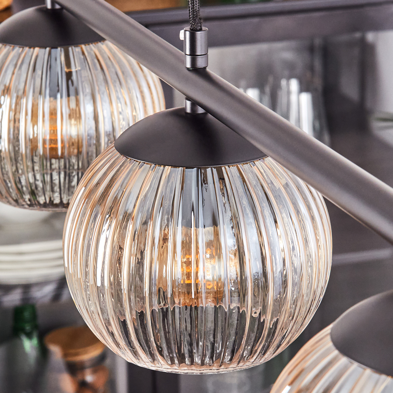 Nahaufnahme einer modernen Leuchte mit drei Glas-Kugelschirm. Jeder gerippte Glasschirm hat eine warme Glühbirne und einen schwarzen Metallrahmen.