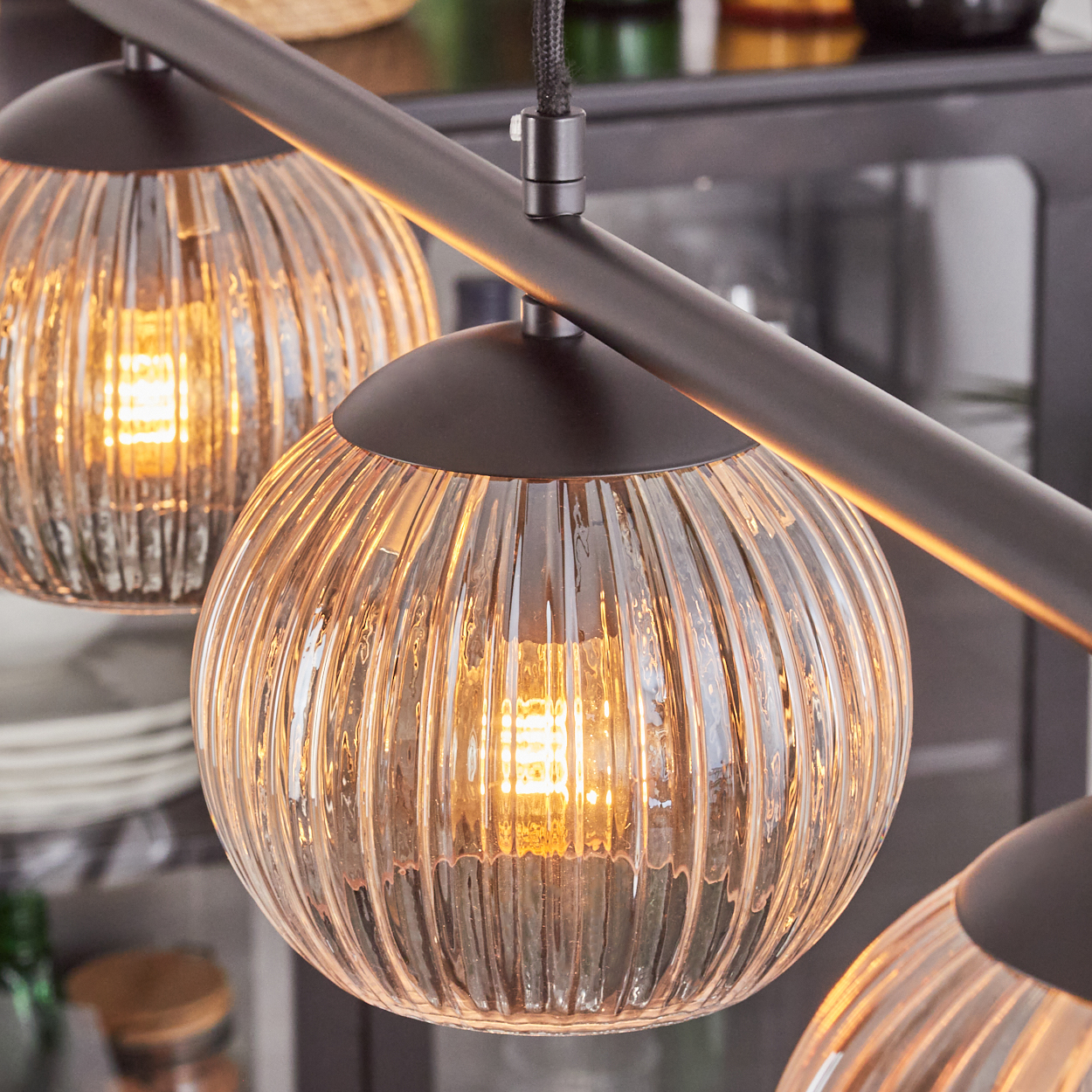 Nahaufnahme einer modernen Leuchte mit drei Glasschirmen. Die Schirme haben ein geriffeltes Design und sind von innen beleuchtet.