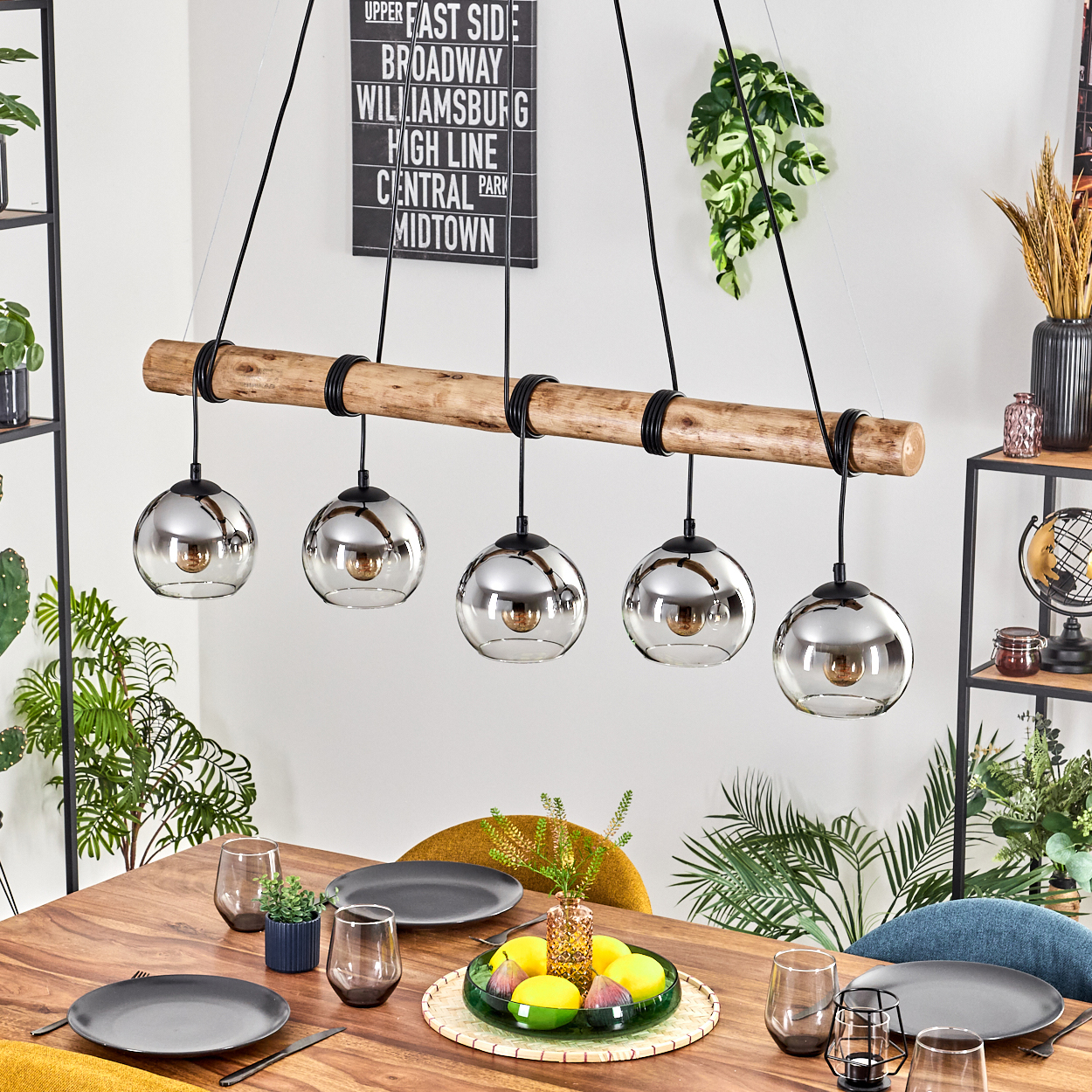 Esszimmer mit Holztisch, Leuchte mit Glaskugeln, Tellern, Gläsern und Dekoration.