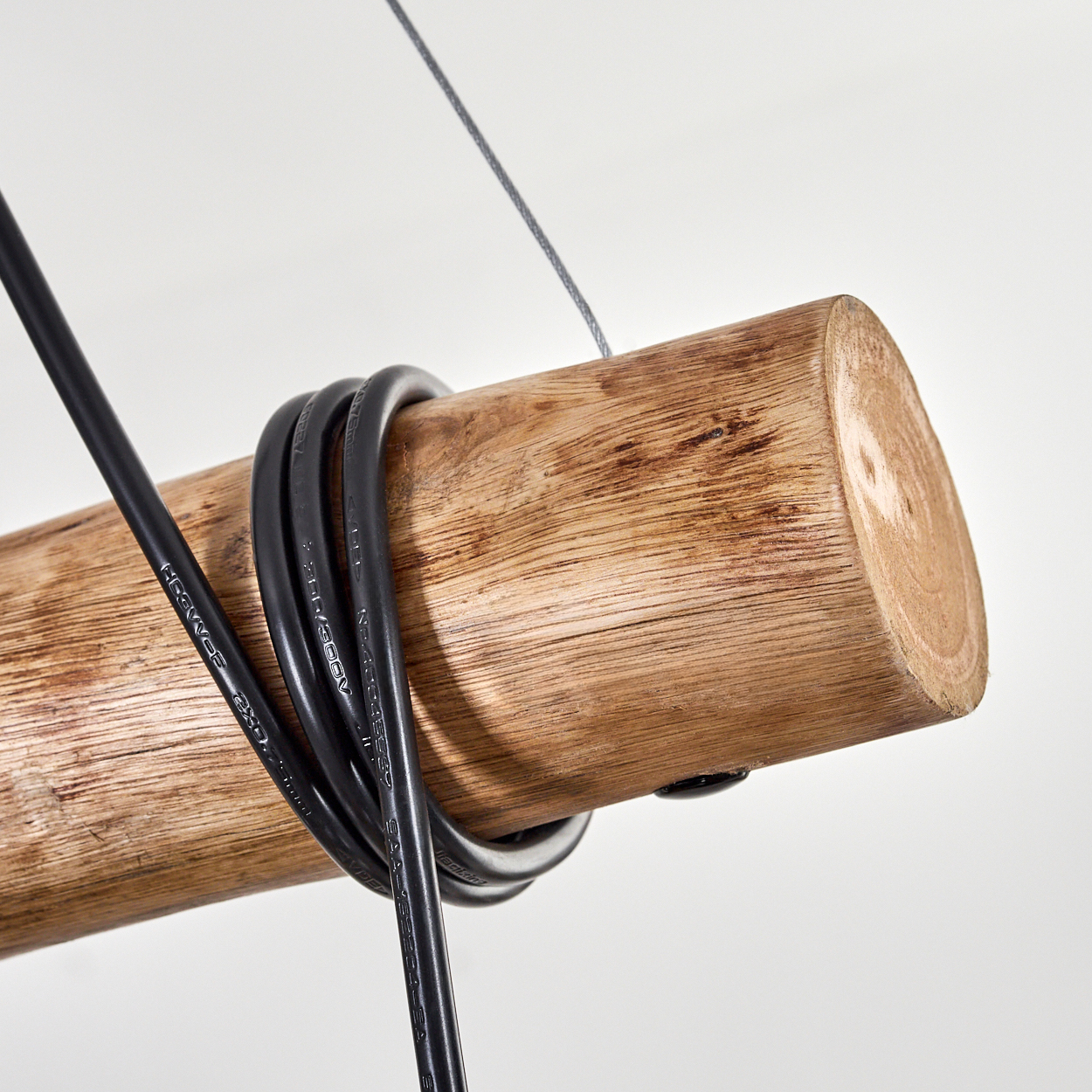 Nahaufnahme eines Holzbalkens mit einem schwarzen Kabel darum. Ein grauer Draht hängt von oben herab.