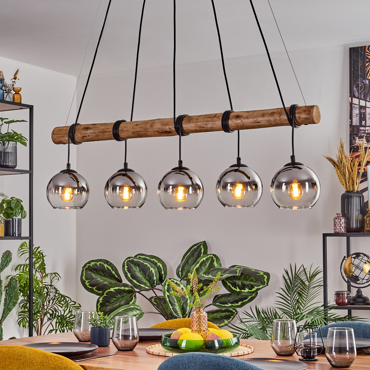 Esszimmer mit Holzbalken-Kronleuchter mit fünf Glaskugelleuchten. Darunter ein Tisch mit Gläsern und Pflanzen.