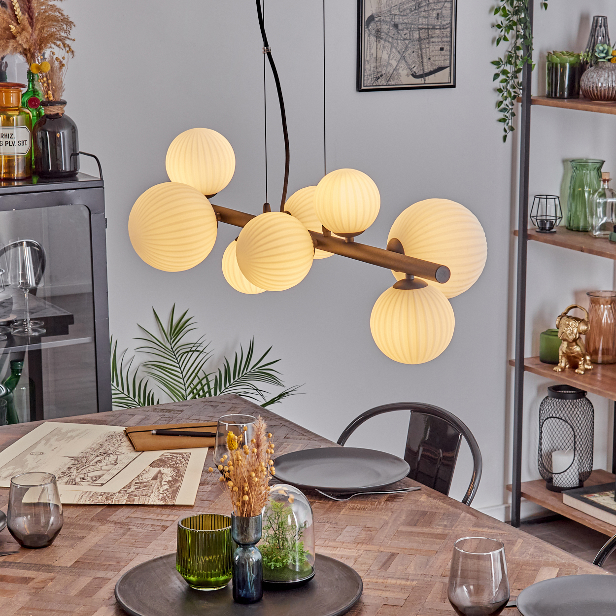 Esszimmer mit Holztisch, Hängelampe, Tellern, Gläsern und Dekoration. Regale mit Vasen befinden sich rechts.