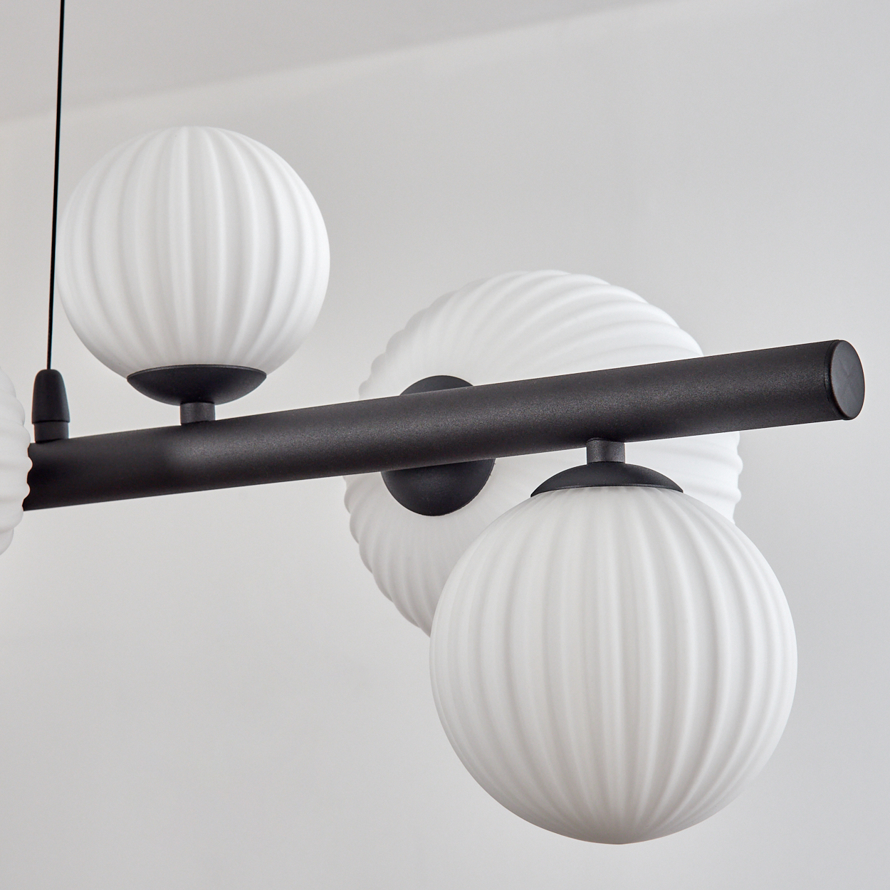 Eine moderne Deckenlampe mit weißen Kugeln und einer schwarzen Stange vor einer weißen Wand. Die Kugeln haben ein geripptes Design.