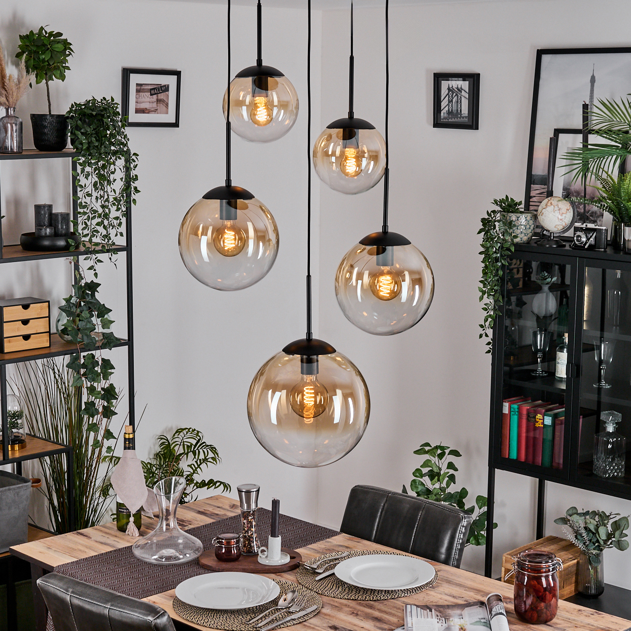 Esszimmer mit Holztisch, Glaskugel-Pendelleuchten und Dekoration. Pflanzen und Regale im Hintergrund.