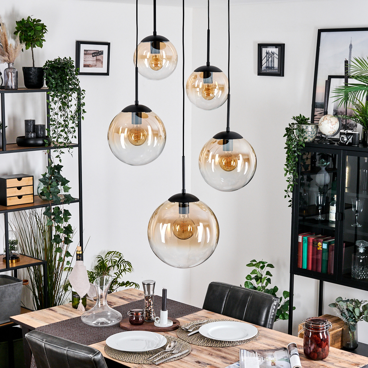 Esszimmer mit Holztisch, Glaskugellampen und Dekoration. Teller und Besteck sind gedeckt. Pflanzen und Bilder schmücken die Wände.