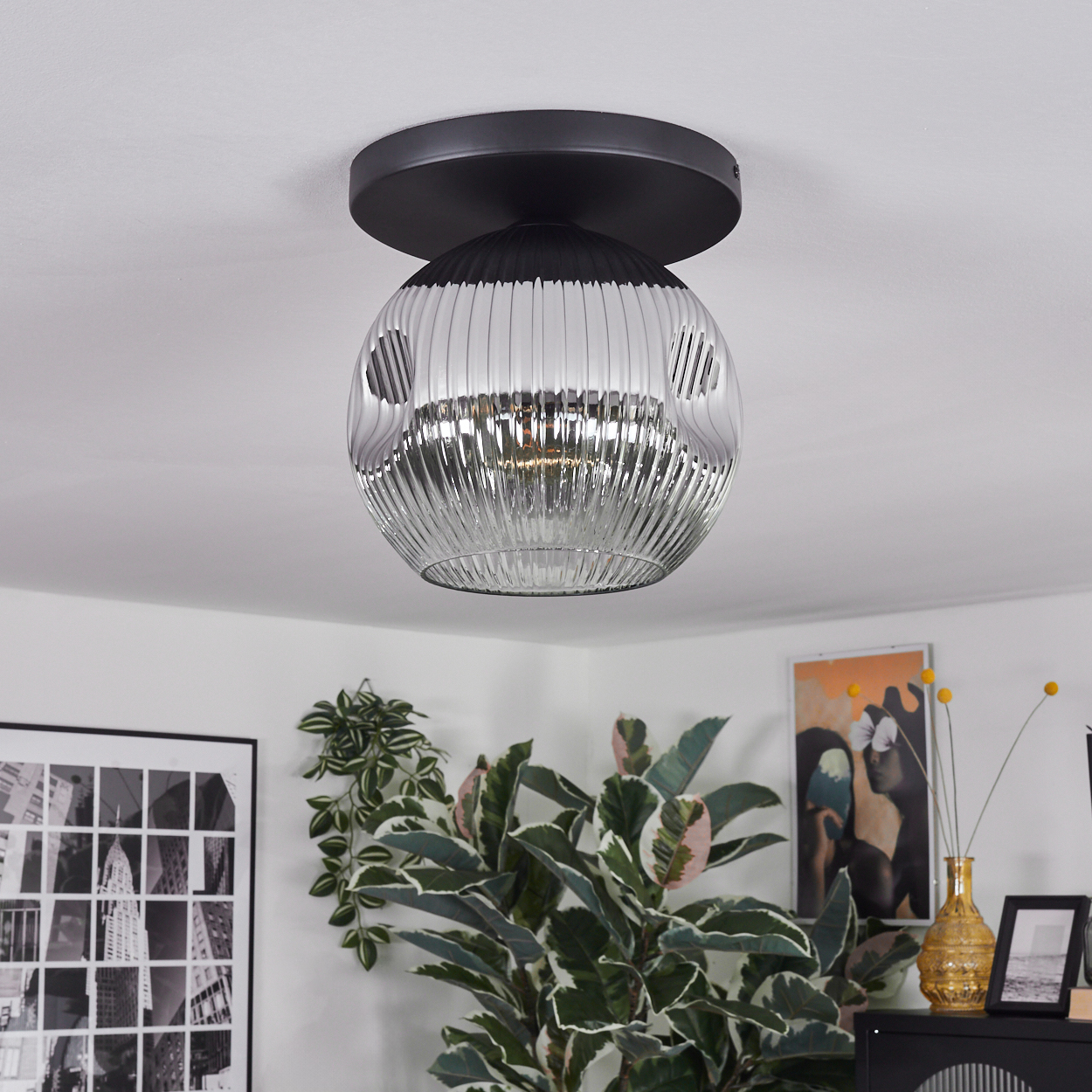 Eine moderne Deckenleuchte mit Glasschirm. Im Hintergrund befinden sich eine Pflanze und Kunstwerke.