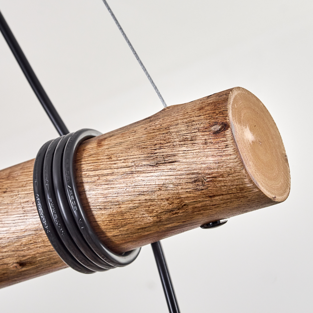 Holzstamm mit schwarzem Kabel, das darum gewickelt ist, an einem Draht vor weißem Hintergrund aufgehängt.