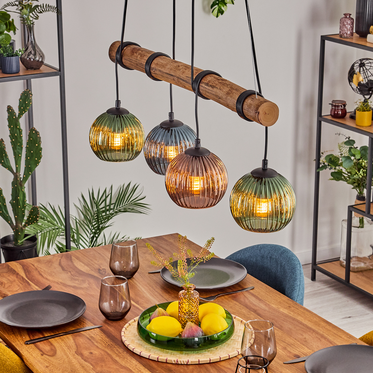 Esstisch mit vier Hängelampen, Glas, Zitronen und einem Holztisch. Regale mit Pflanzen im Hintergrund.