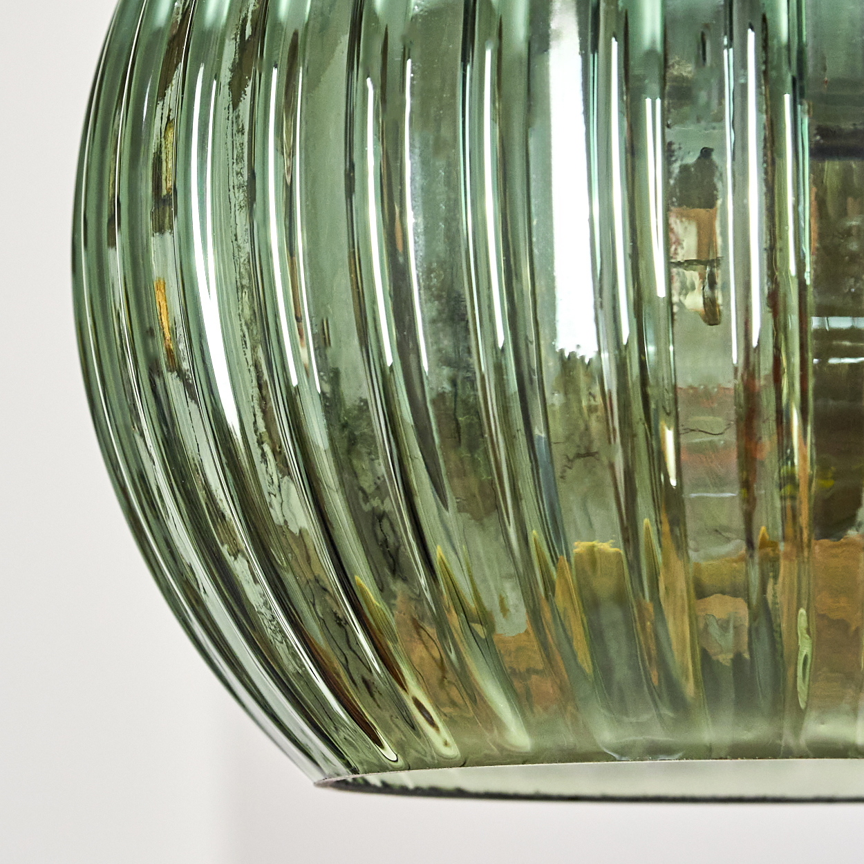 Nahaufnahme eines grünen, gerippten Glasobjekts. Das Glas reflektiert Licht und die Umgebung. Weißer Hintergrund.
