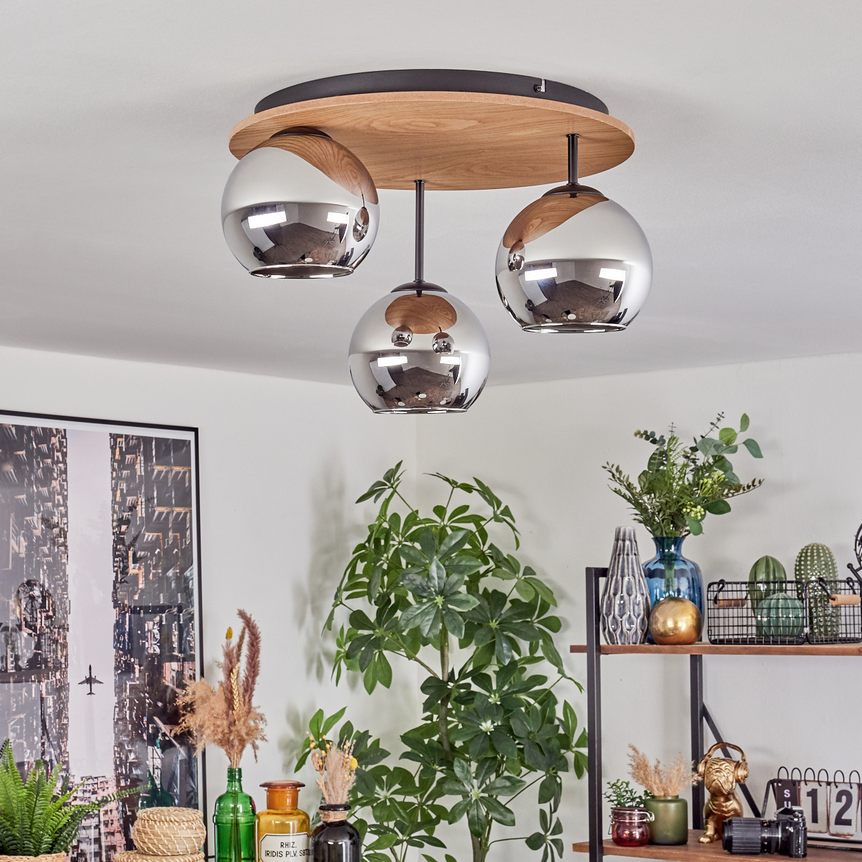 Deckenlampe mit drei Chromkugeln, Holzsockel. Pflanzen, Dekorationen und ein Stadtbildfoto im Raum.