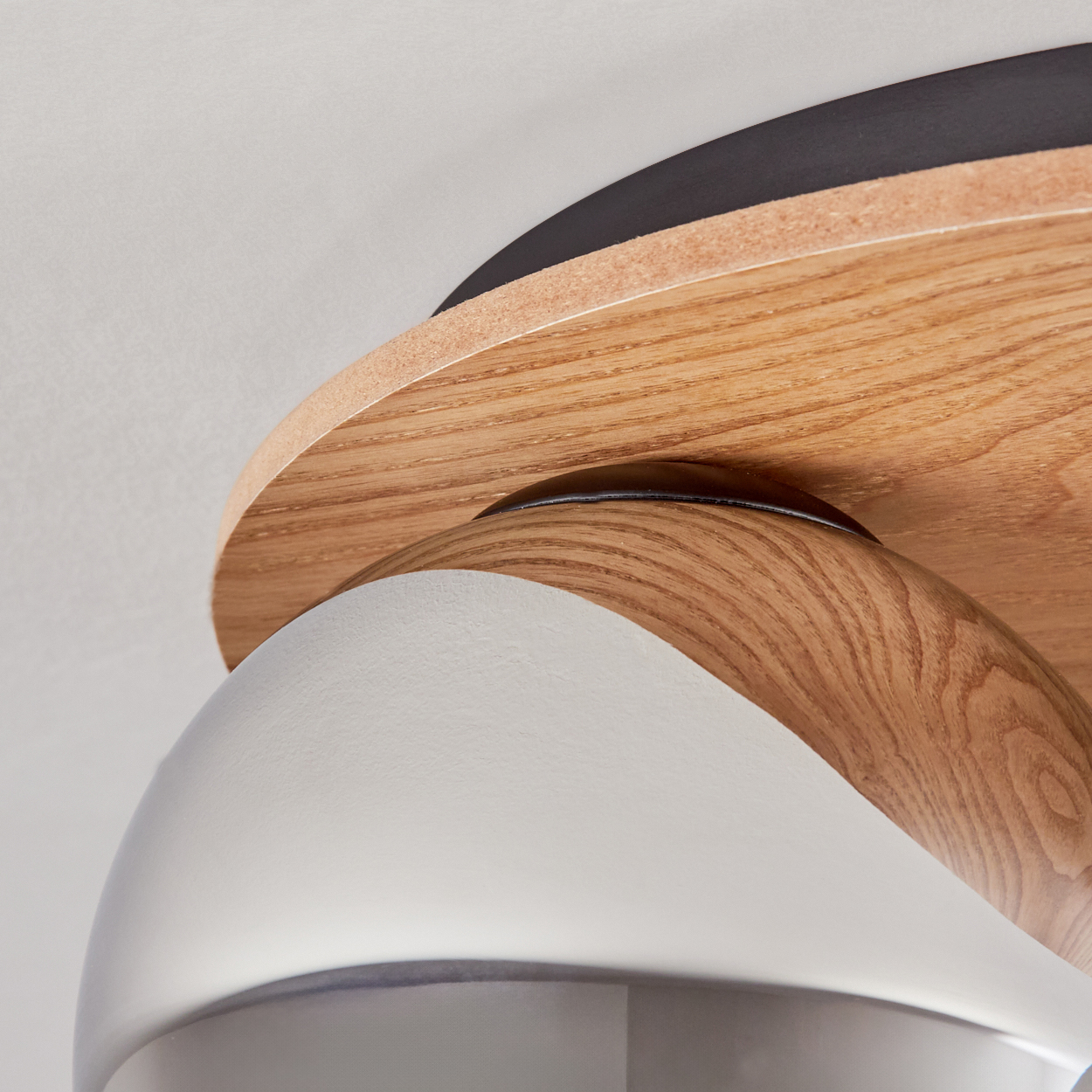 Nahaufnahme einer Holzdeckenlampe. Sie hat einen Holzschirm und ein weißes, gebogenes Element, mit einer weißen Decke im Hintergrund.
