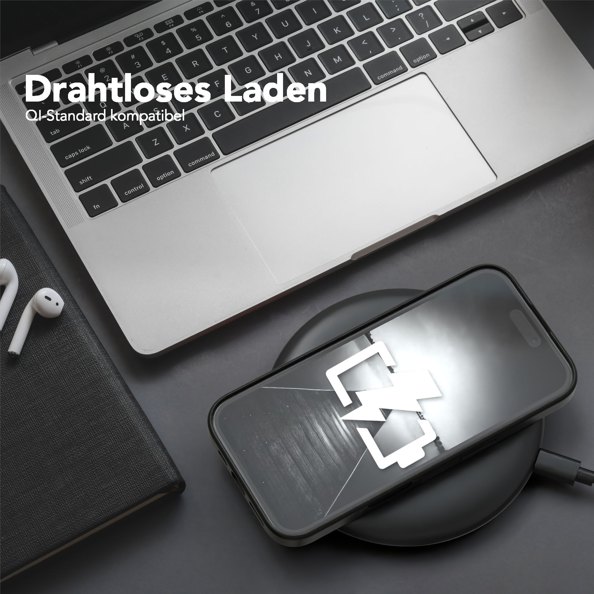Ein Telefon, das drahtlos auf einem Pad neben einem Laptop geladen wird. AirPods und ein Notizbuch sind ebenfalls vorhanden.