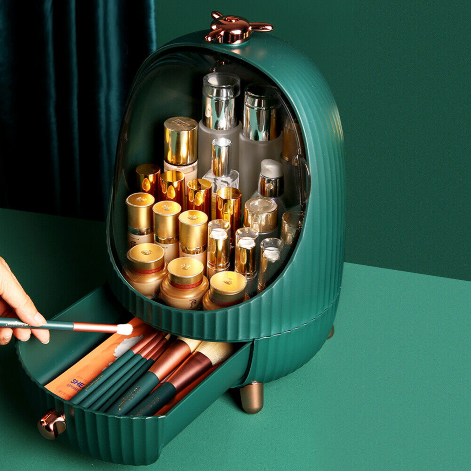 Ein grüner Make-up-Organizer mit offener Schublade. Er enthält Pinsel und Kosmetika. Hand, die einen Pinsel hält.